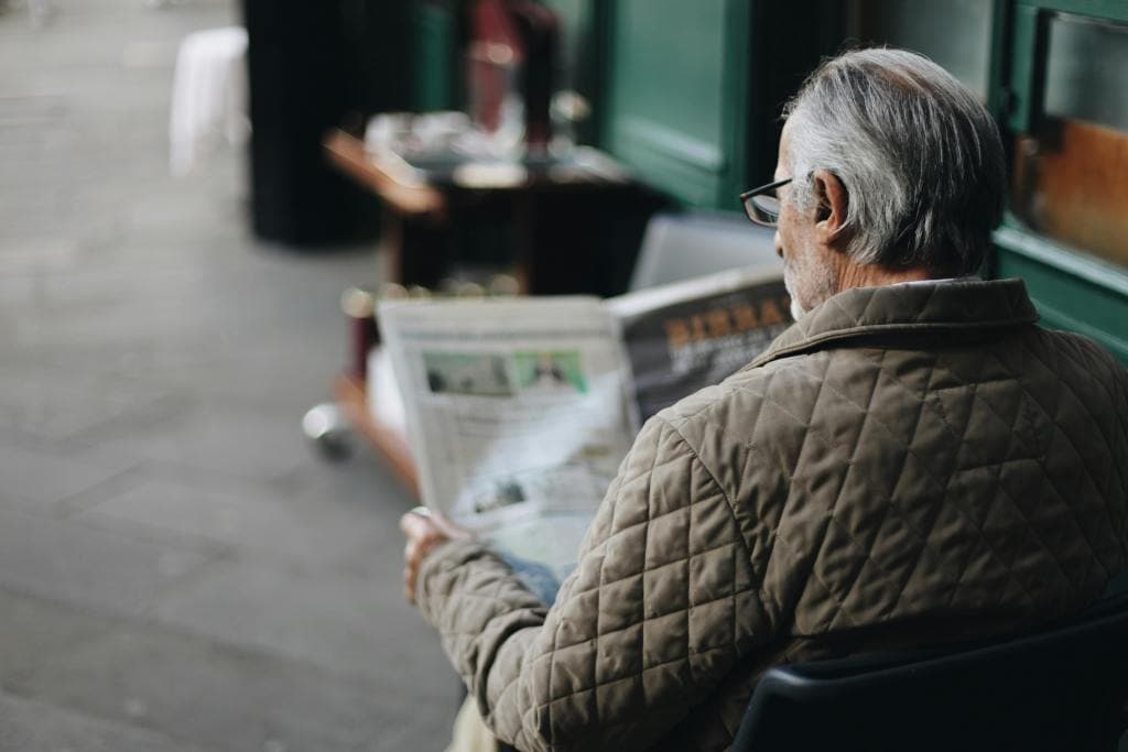 An elderly person reading with assistive support.