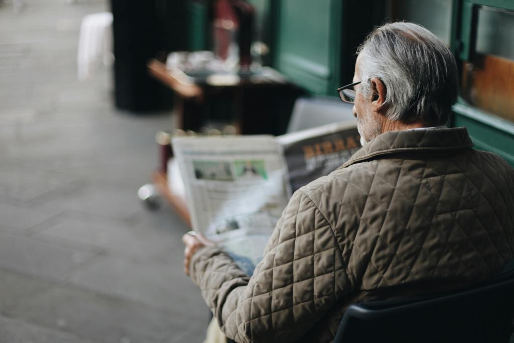 Elderly man reading a newspaper in an outdoor cafe setting, enjoying a peaceful moment.