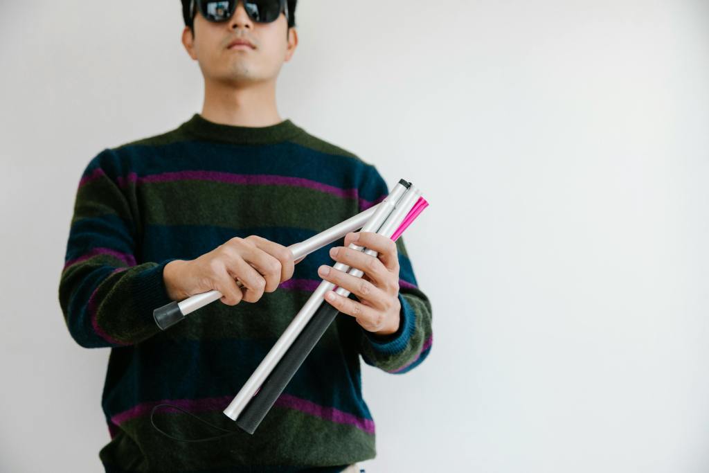 Man wearing sunglasses assembling a walking cane, symbolizing support for visual impairment.